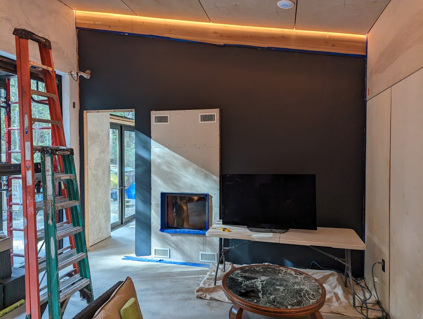 Fortress Foster living room — leathered concrete floor, lime plaster walls, amber accent lighting, fireplace niche, forest through glass doors